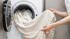 Someone putting a throw blanket into a washing machine
