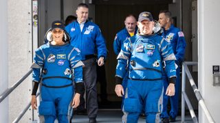 Dwóch astronautów ubranych w niebieskie skafandry Boeinga opuszcza budynek przygotowań do startu NASA