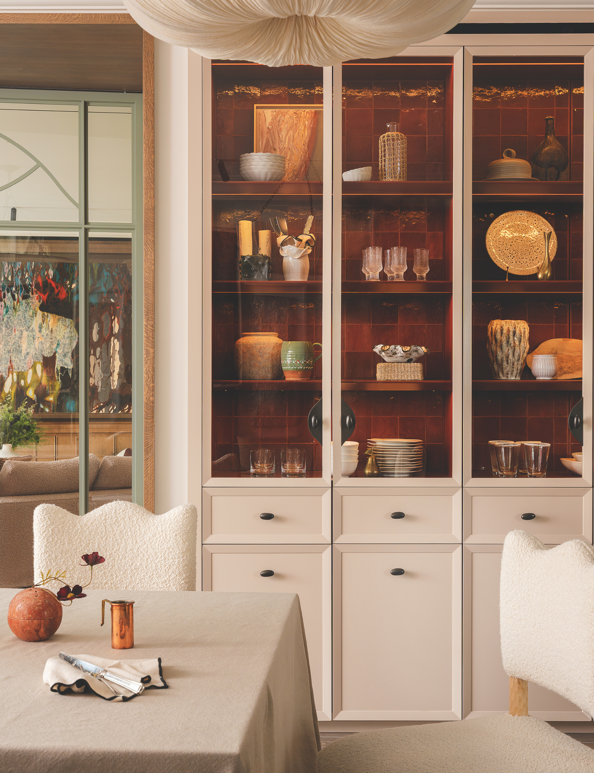 Neutral dining room area featuring a three-panel curio shelf of assorted tableware and wave-bordered dining chairs