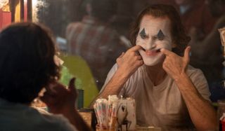 Joker Arthur forcing a smile in the mirror, in full makeup