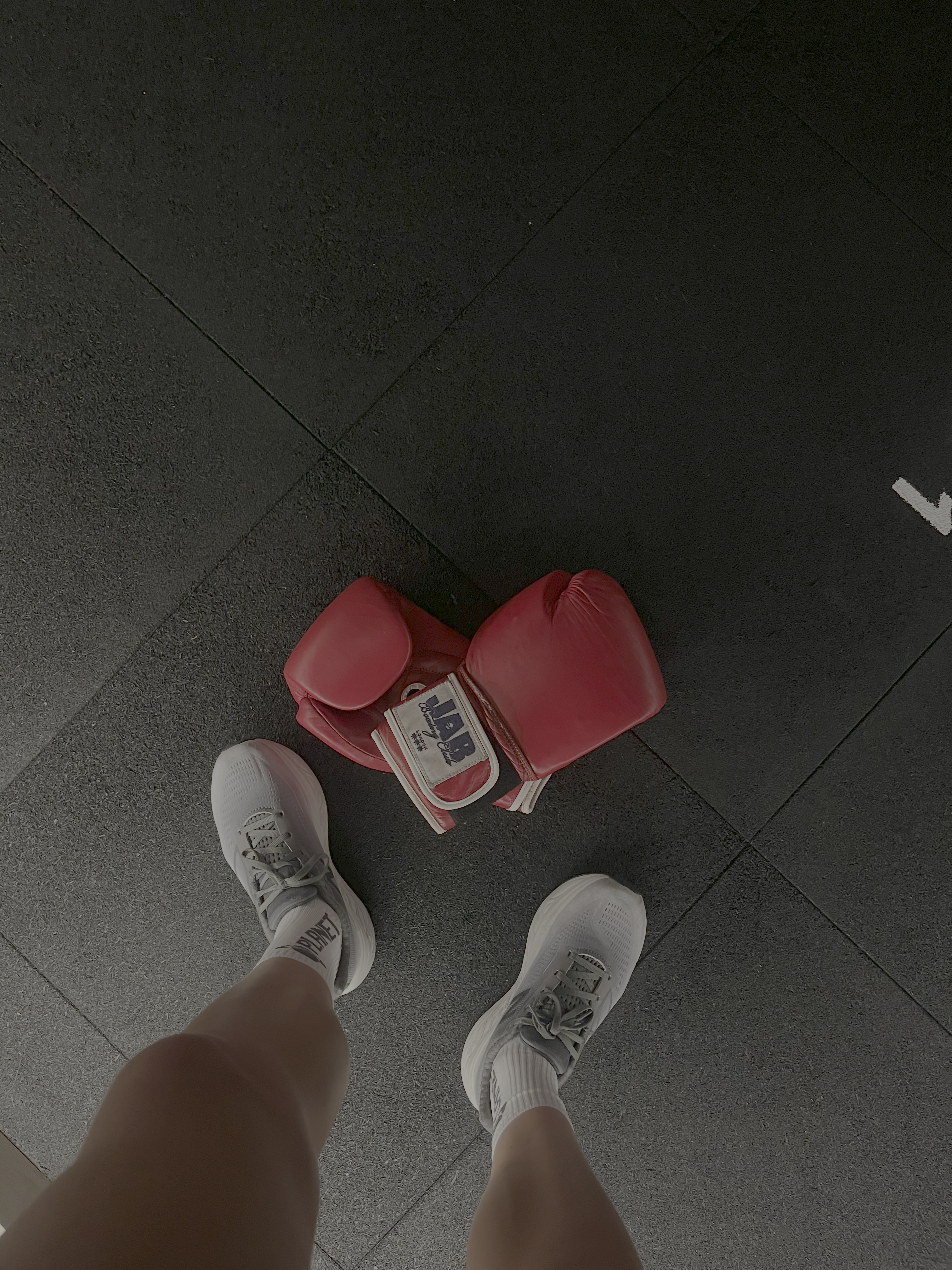 A pair of boxing gloves lying on the floor with a woman's feet in trainers