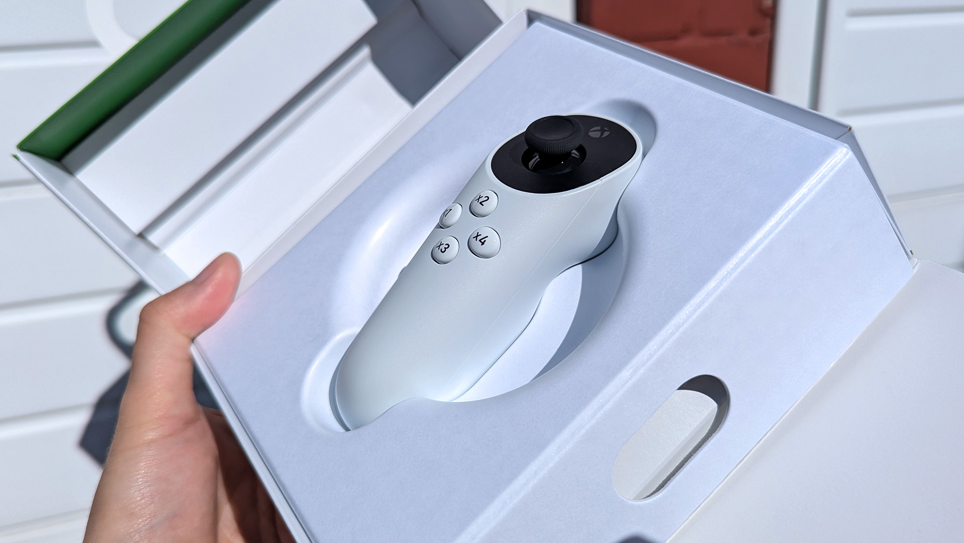 Xbox Adaptive Joystick held in hand, in its open retail box