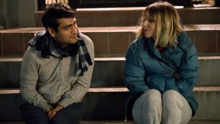 A still from the movie The Big Sick in which the two main characters Kumail and Emily are sitting on steps. Kumail is wearing a grey hoodie and a scarf and Emily is wearing a blue coat.