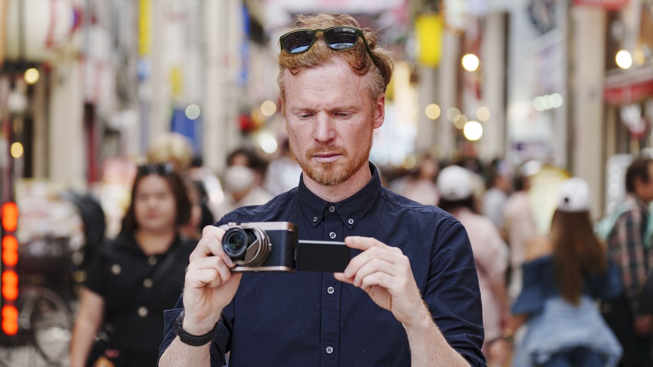 Man holding the Panasonic Lumix L10 compact camera in an urban setting of Japan