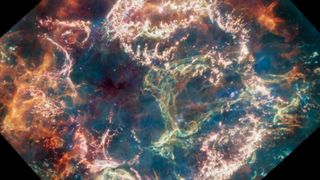 A wall of green gas blooms at the center of a colorful supernova remnant