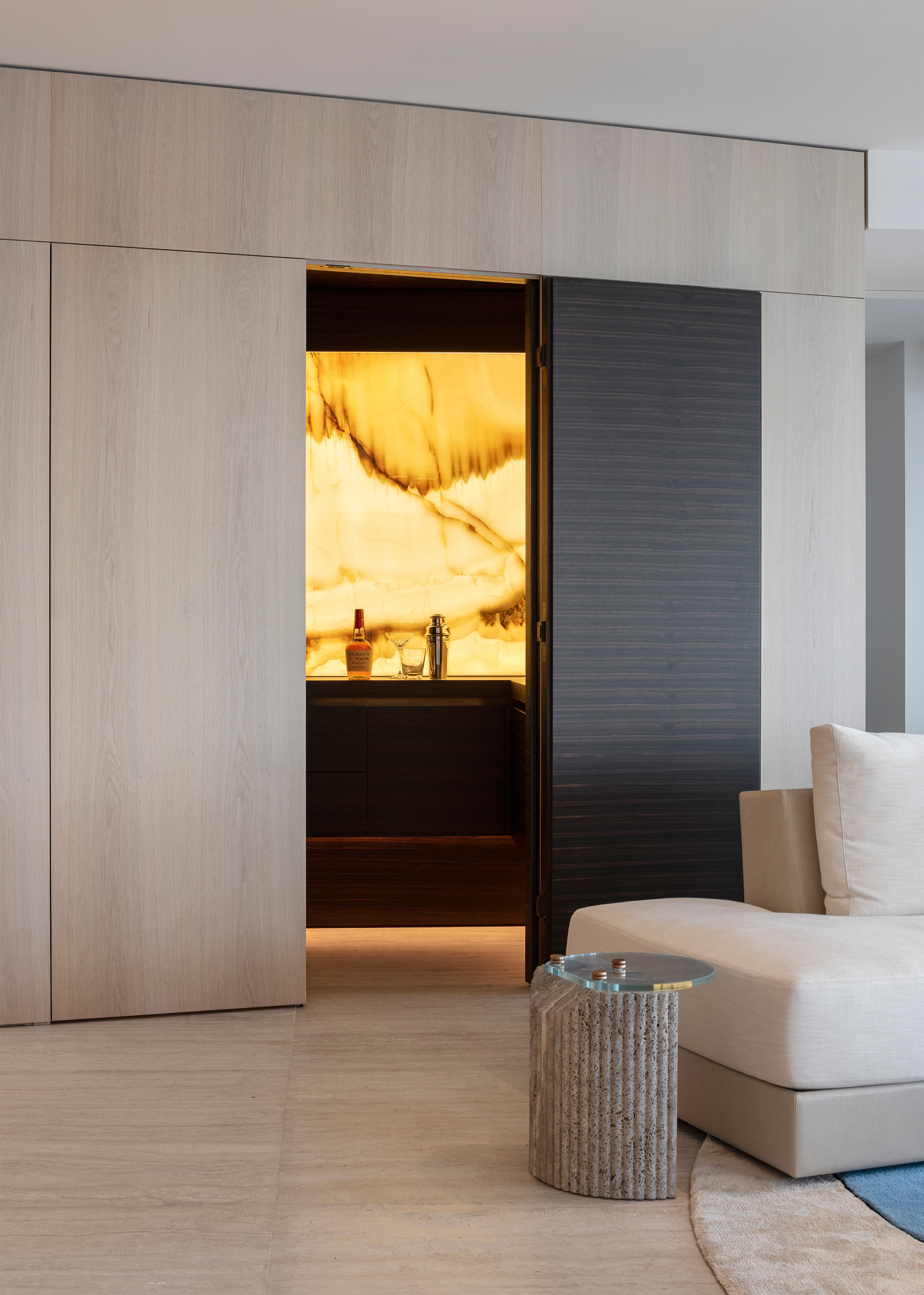 Bar behind a white oak panelled opening with a black door, leading to a backlit backsplash