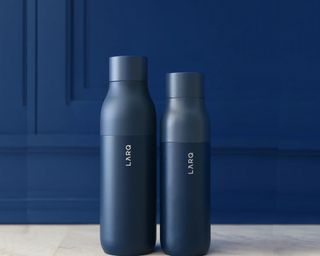 A pair of navy blue metal water bottles against a dark blue wall