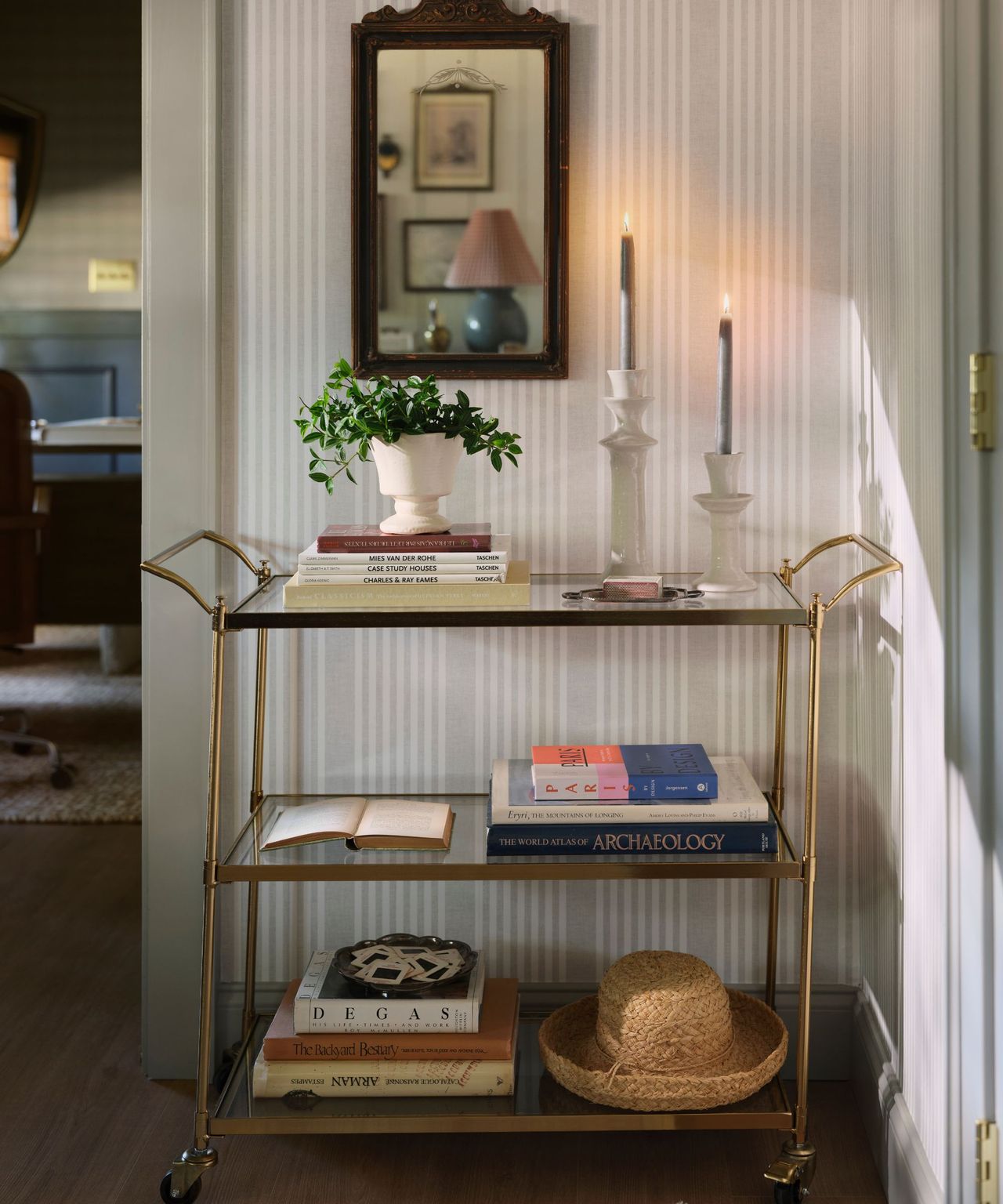 Home office with striped wallpaper and bar cart with decor, stacks of books and candles