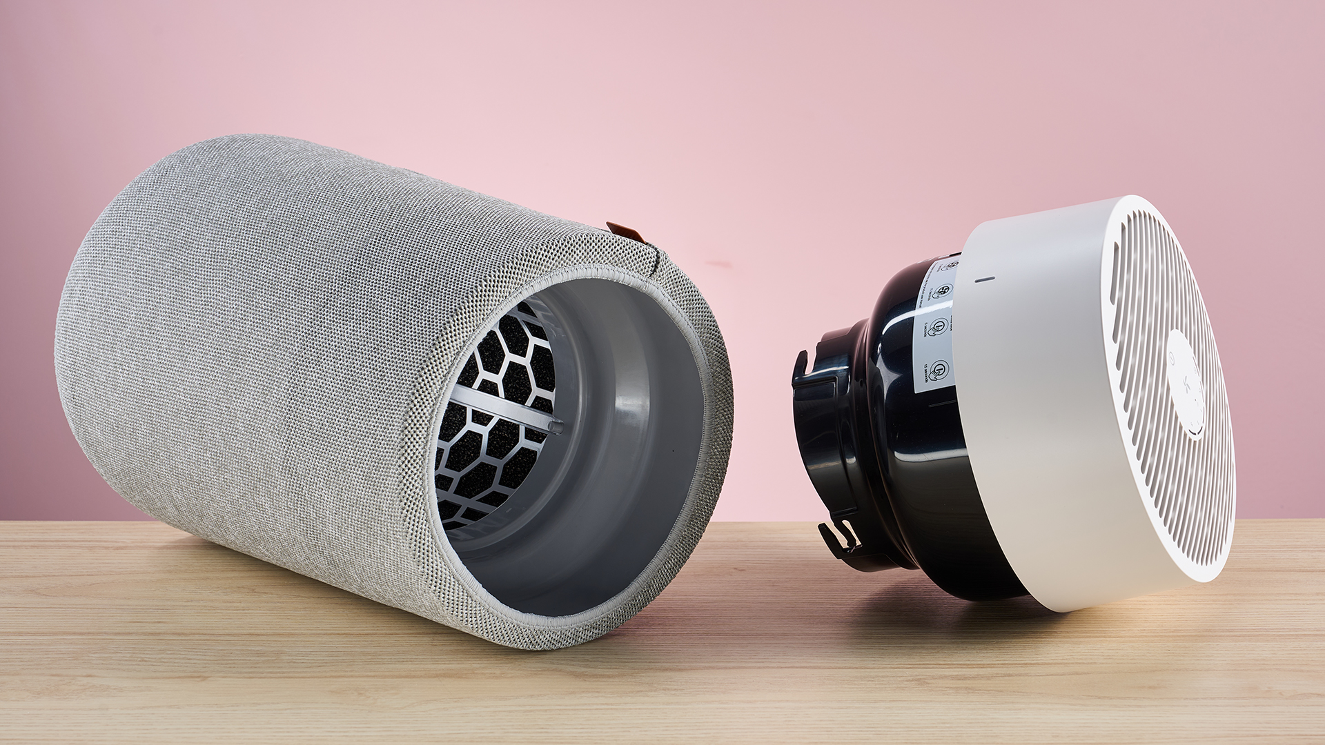 The large Blueair air purifier sits on its side with the top removed on a wood surface against a pink background.