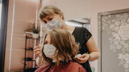 Hairdresser in a salon wearing a mask and styling hair into a wavy bob