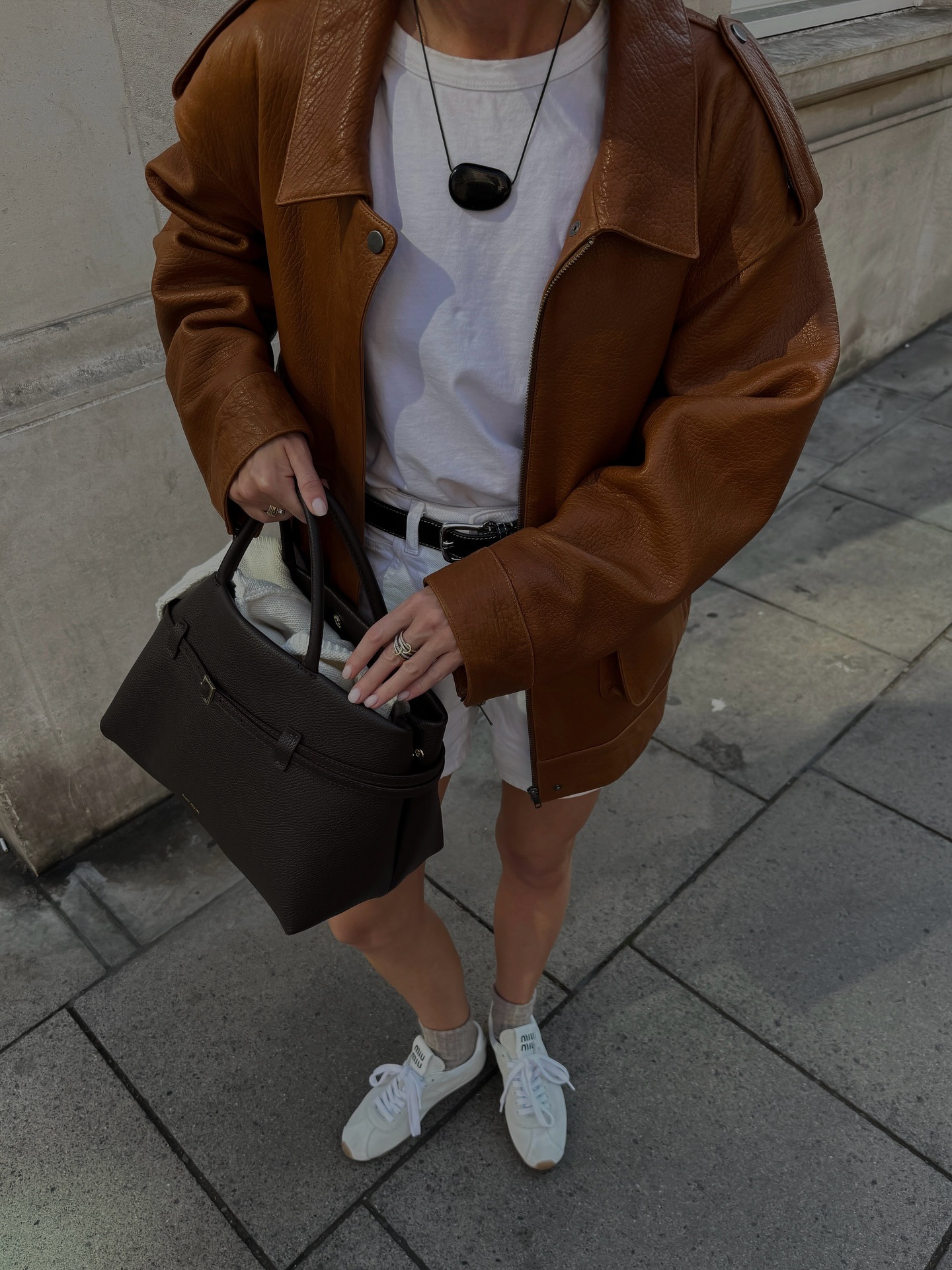 Woman wearing black Heaven Mayhem julia stone necklace with white t-shirt, suede jacket, black bag, and white tennis shoes.