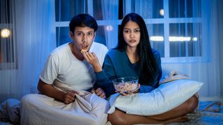 man and woman sharing bowl of snacks as they watch a movie