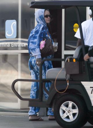 Rihanna arrives at an airport wearing a tie dye sweatsuit and three bags