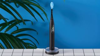 a black electric toothbrush with a small touchscreen and a blue toothbrush head and a square charging stand