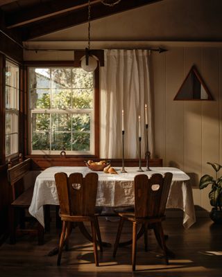 A rustic dining room with wooden chairs, a linen dining cloth on the table, and candle sticks on the table