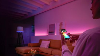 The best Philips Hue deals 2022, image shows living room bathed in pink light while a person uses the Hue app to adjust it
