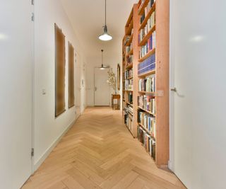 long narrow hallway painted white with wooden floor and slim wooden bookcase built along one wall