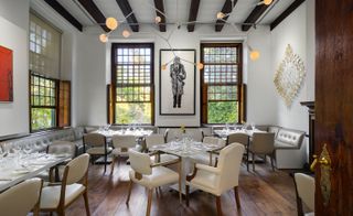 Dining section of the restaurant with leather seating with tables dressed, long brown windows, artstic hanging lights and walls adorned in art