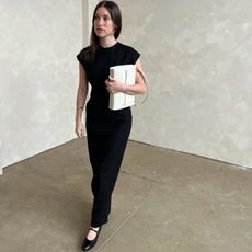 woman wearing black tank maxi dress with black Mary Jane ballet flat holding white structured shoulder bag in front of marble wall