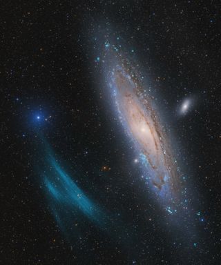 A bright galaxy hangs in space near a smear of blue nebulas gas and beside a mush smaller, more distant galaxy.