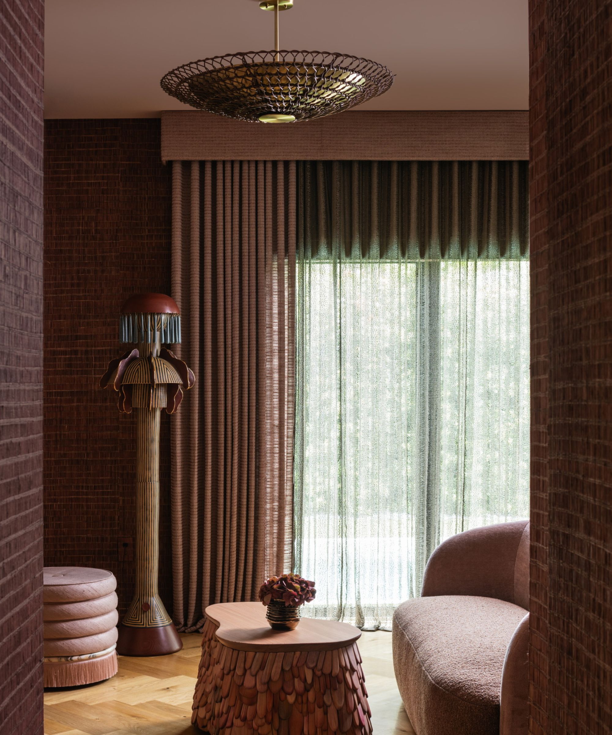 a cozy sitting room with long drapes covering the windows, a textured wall paper, and furniture and other decor in a deep clay color