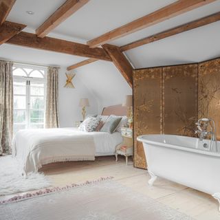 attic bedroom with exposed beams, freestanding bathtub and large french windows