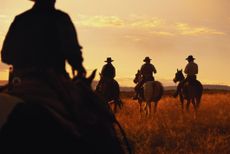 a group of cowboys on horses in a field heading off into the sunset