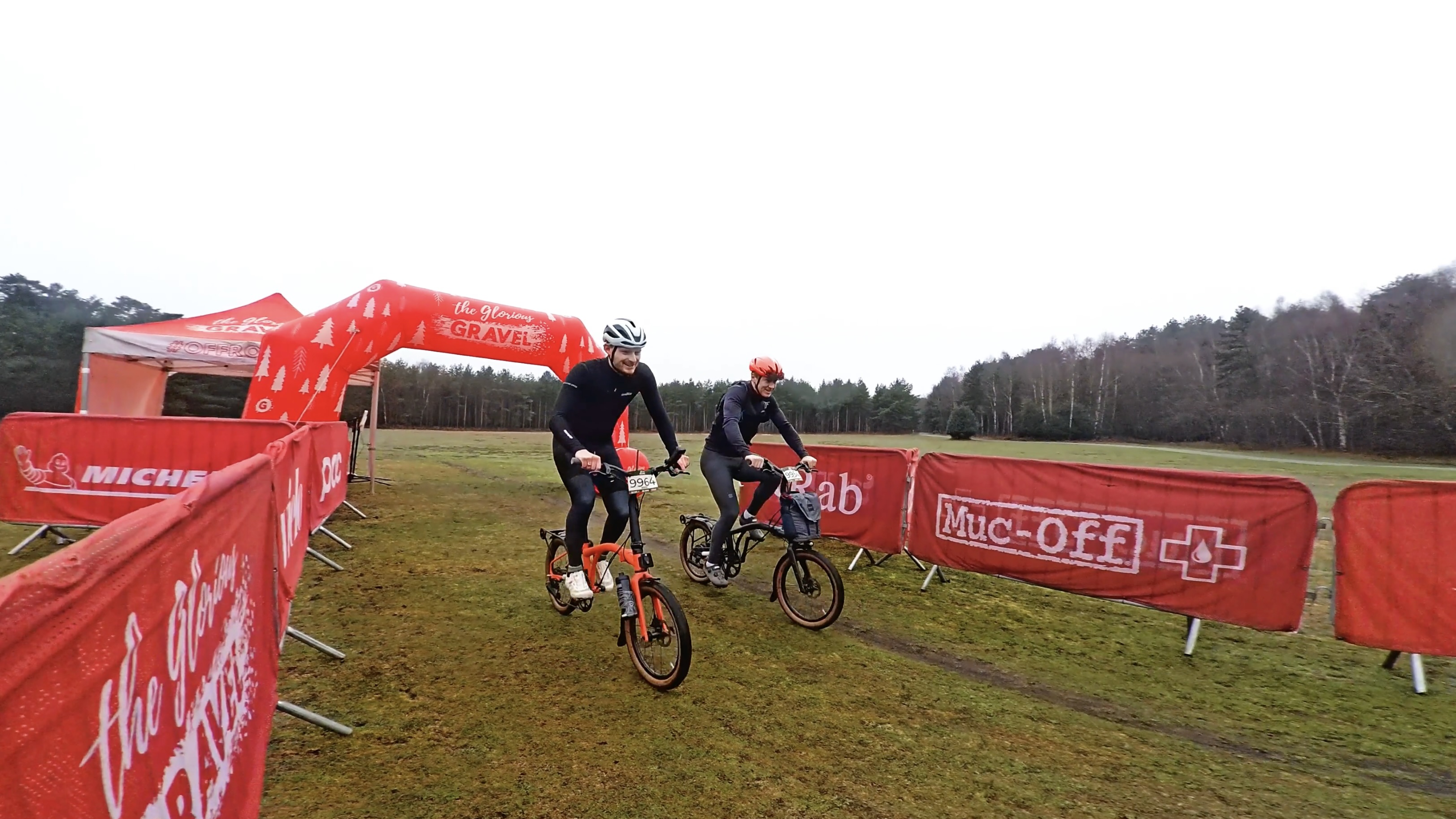 An orange Brompton covered in mud on a light gravel track