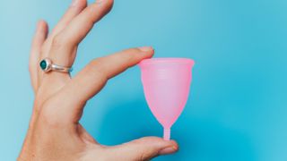 woman holding pink menstrual cup against blue background
