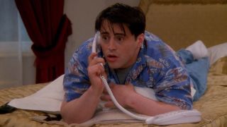 Matt LeBlanc plays Joey Tribbiani on Friends, shown here talking on the phone while lying on a bed in a hotel.