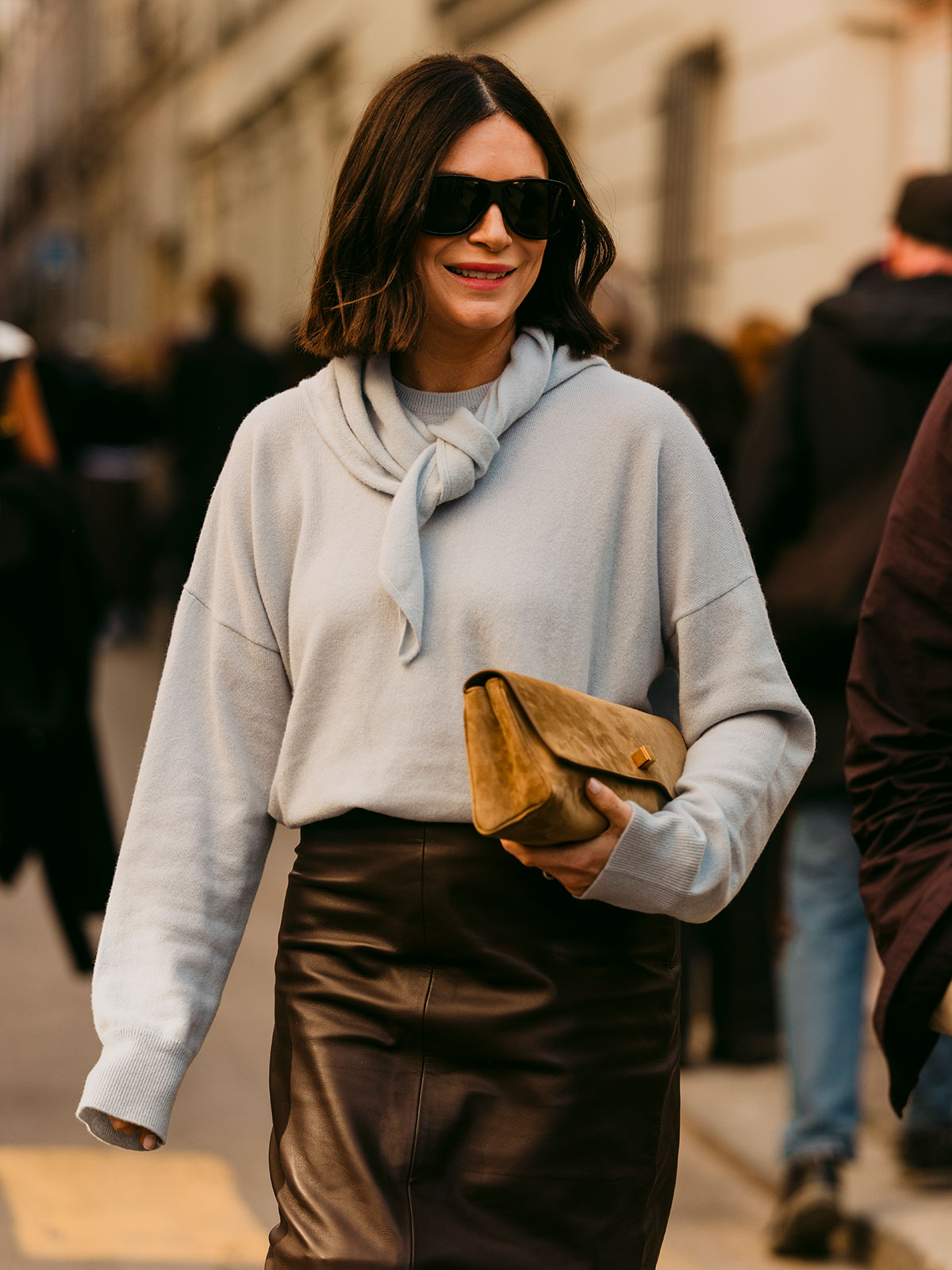 Woman wearing a crewneck sweater, a matching scarf, and a leather skirt.