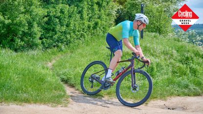 A lone rider in a green jersey rides a GianT Revolt gravel bike out of woodlands