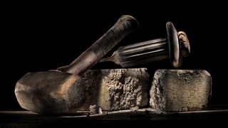A hammer and chisel rest on slabs of stone in front of a black background.