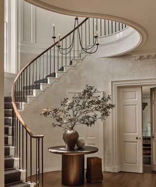 grand hallway with spiral staircase and sidetable with vase and large buch foliage