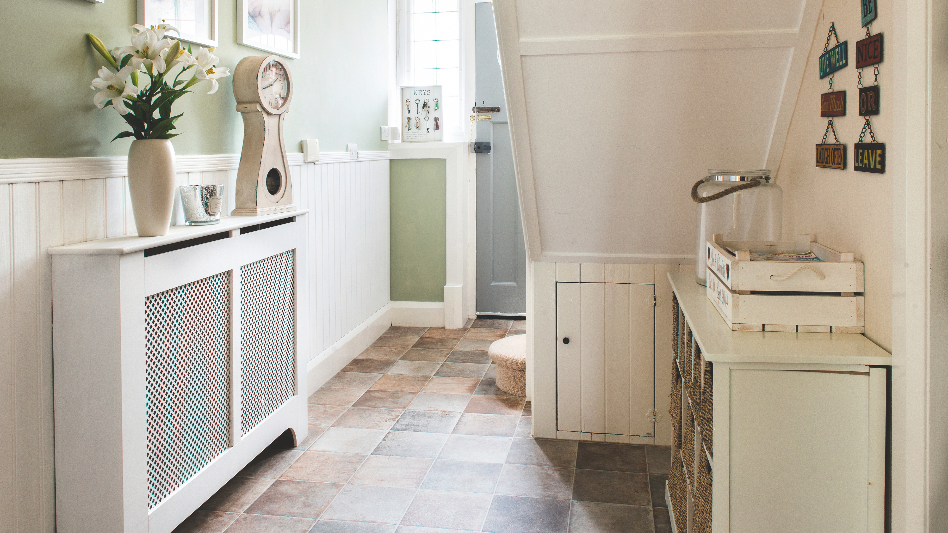 Sage green hallways with a raditor with white shelf and cover. There is a vase and clock on the radiator shelf.