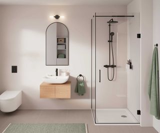 pale pink bathroom with simple shower enclosure and wall hung toilet and wooden vanity unit with arched mirror