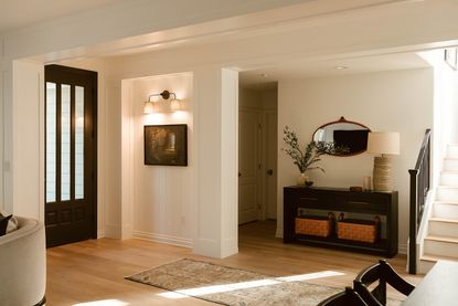 Entryway with console table with baskets, lit up artwork and rug in front of door.