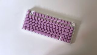 A white keyboard on a white desk with purple Cerakeys keycaps on it