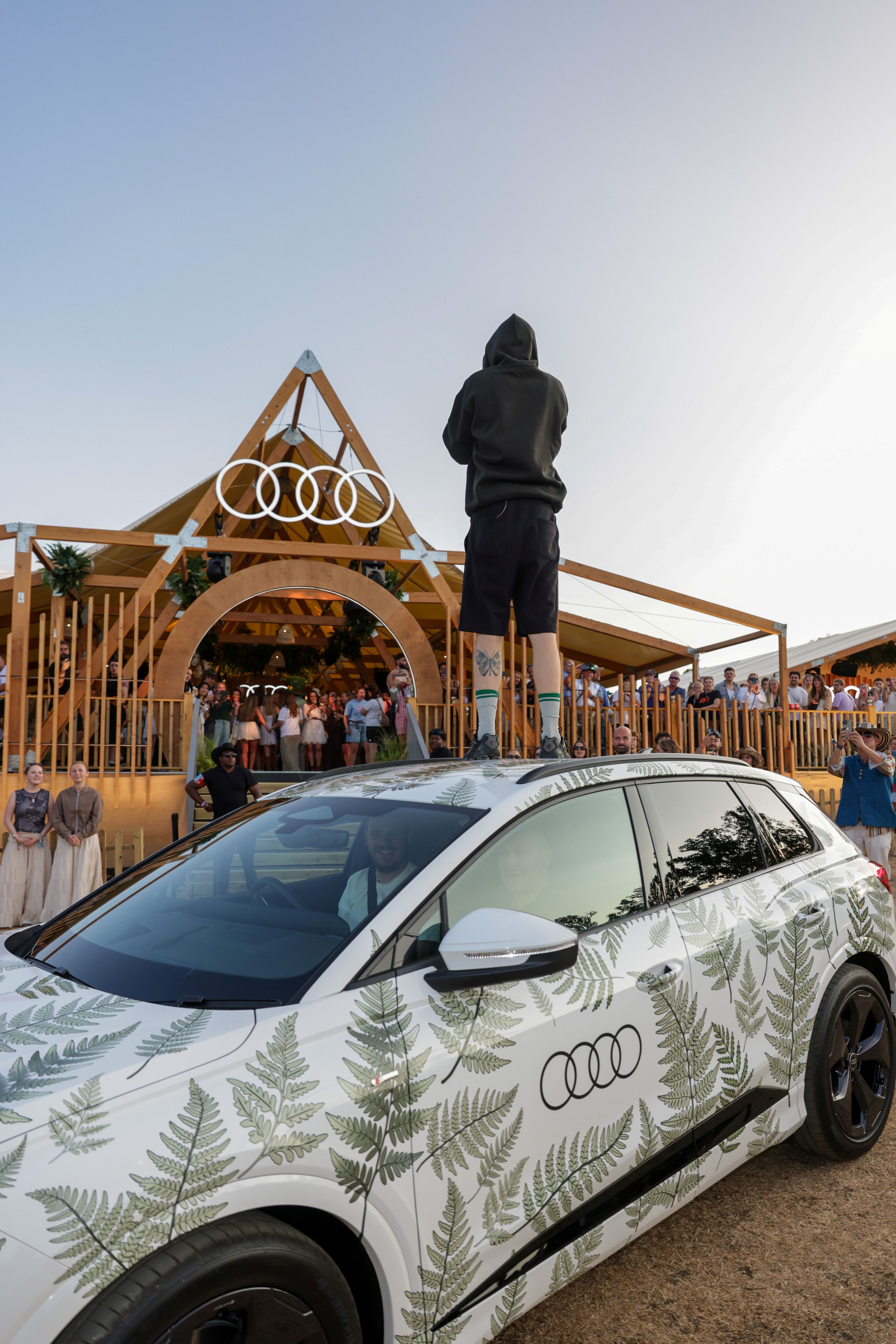 Viewed from behind, Professor Green sings to an audience from the top of an Audi Q4 E-Tron