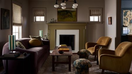 a dark moody living room with a green fireplace, curved dark sofa, two brown armchairs and small floral mushroom stools