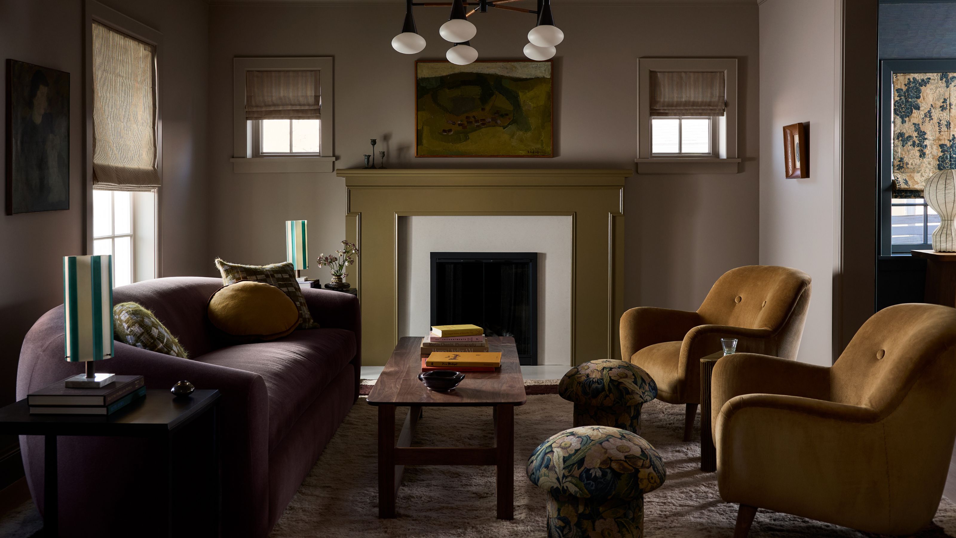 a dark moody living room with a green fireplace, curved dark sofa, two brown armchairs and small floral mushroom stools