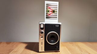 Et Fujifilm Instax Mini Evo-kamera står på et trefarget bord