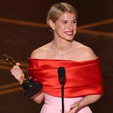 jessie buckley wears a red and pink dress and smiles wide while accepting the oscar for best actress for hamnet at the 2026 academy awards