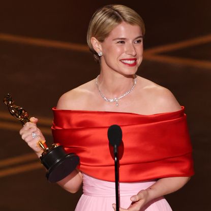 jessie buckley wears a red and pink dress and smiles wide while accepting the oscar for best actress for hamnet at the 2026 academy awards