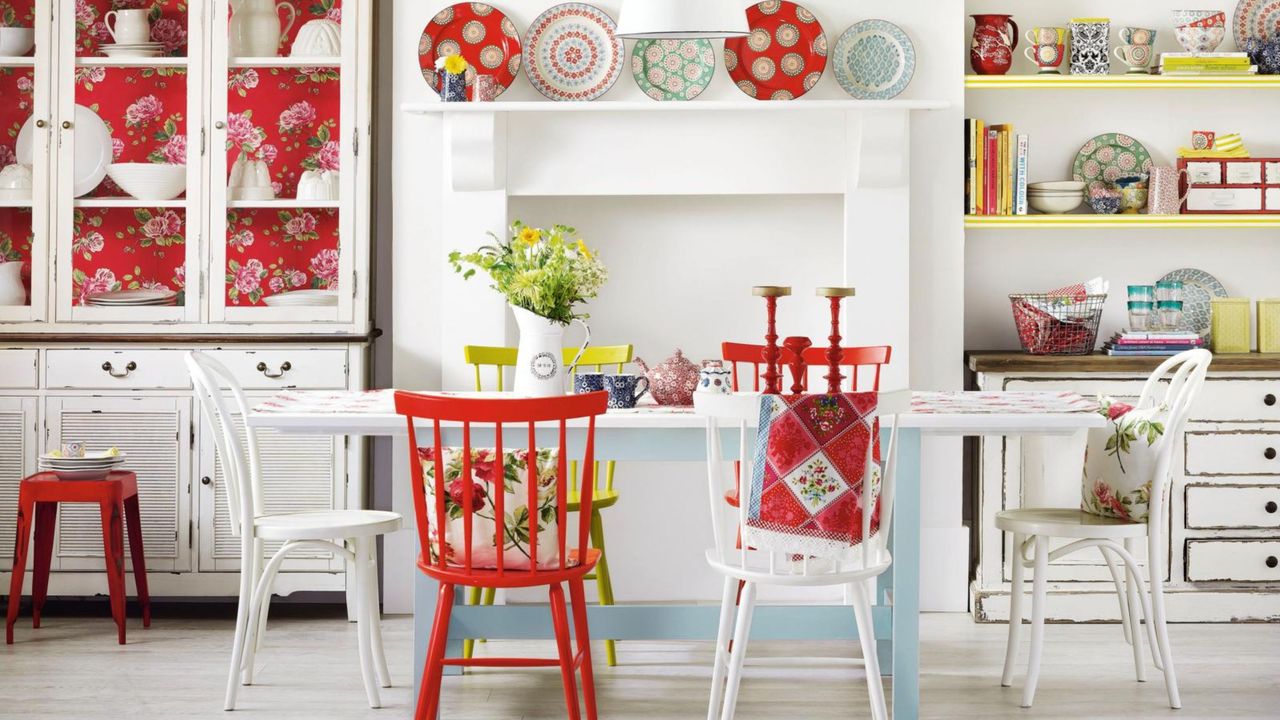 White dining room, distressed mismatching furniture, shabby chic style, blocked in fireplace, vintage dresser with floral wallpapered back unit, mantle displaying antique plates in a grandmillennial interiors style