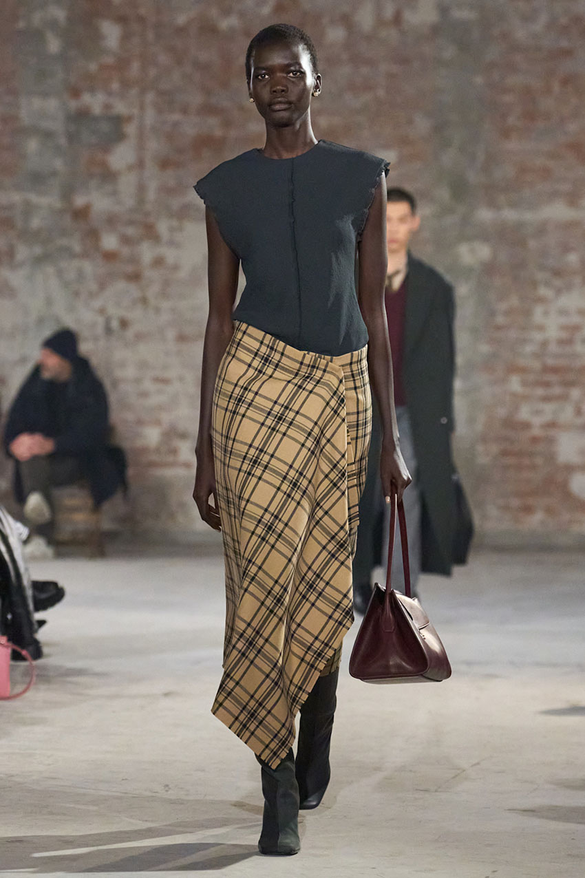 An Ami Paris model wearing a gray top, plaid skirt, and gray knee-high boots