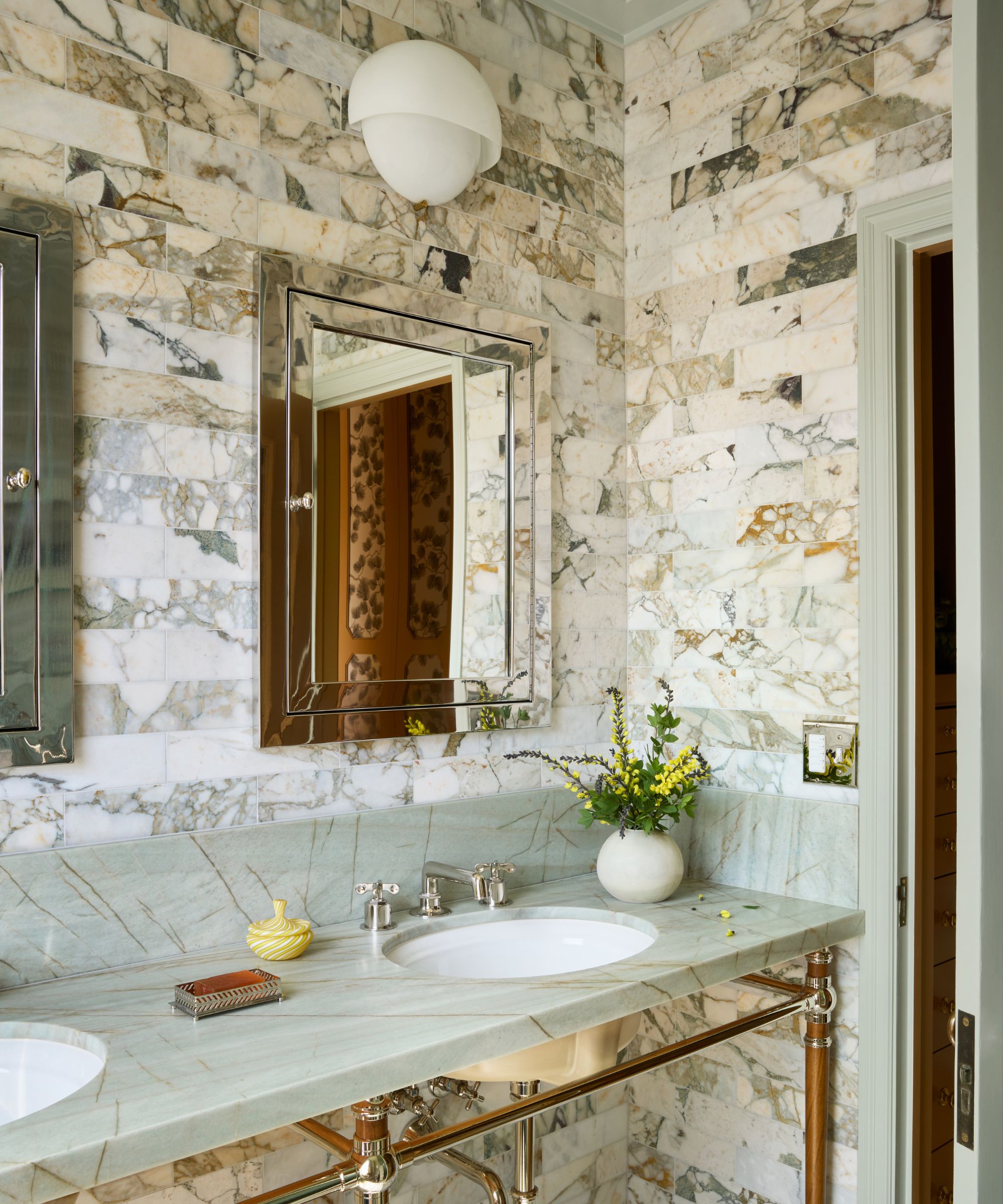 a floor to ceiling marbled tiled bathroom with mint green trim, stone vanity and art decor style mirrors