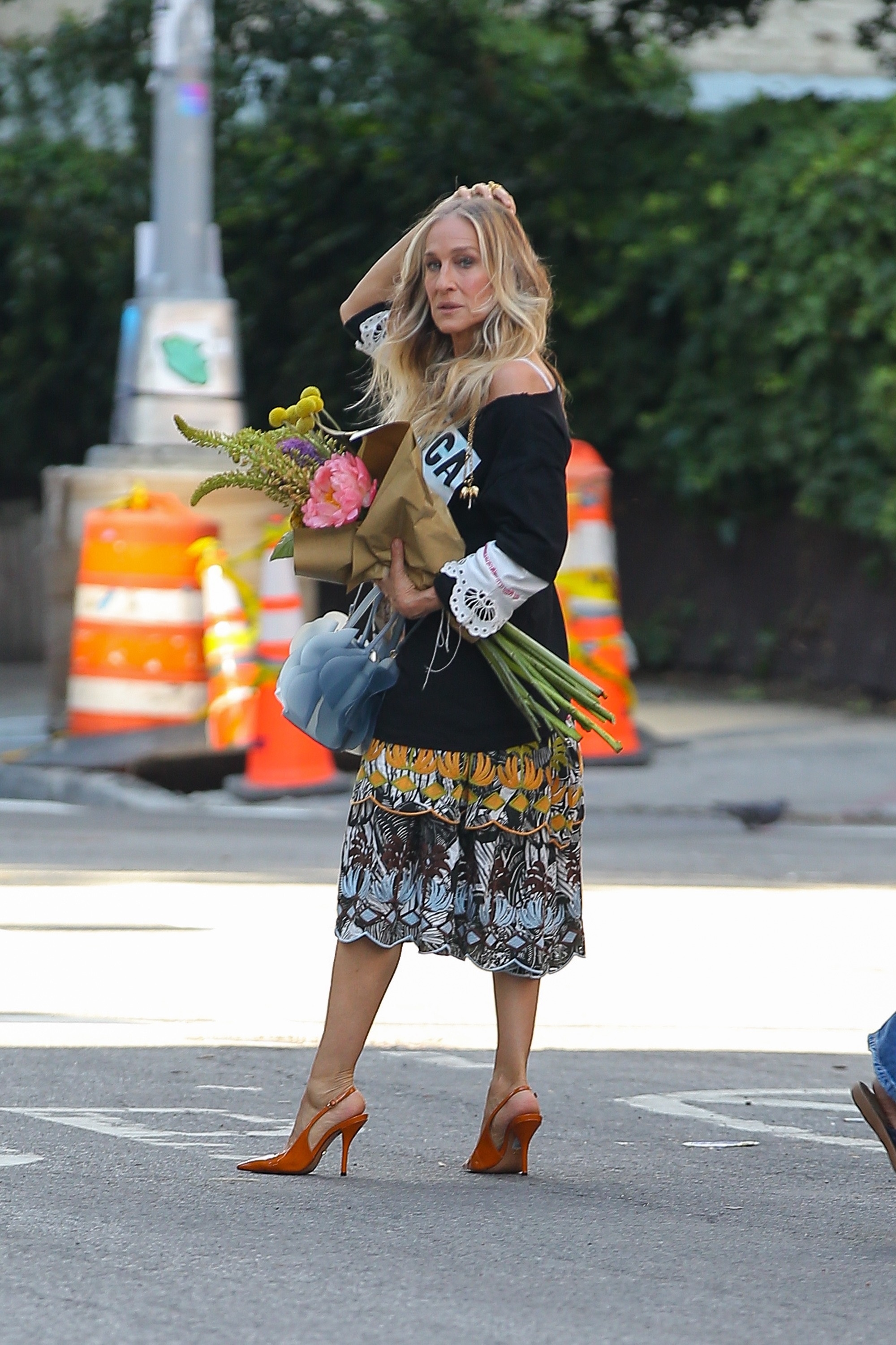Sarah Jessica Parker holds a bouquet of flower in New York wearing a colourful midi skirt with orange slingback heels.