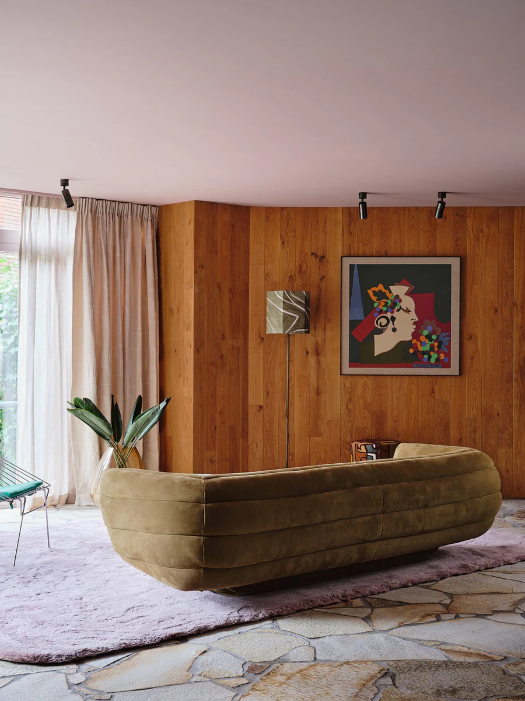 a living room with flagstone floors, a purple rug, a 70s sofa, and wood paneled walls