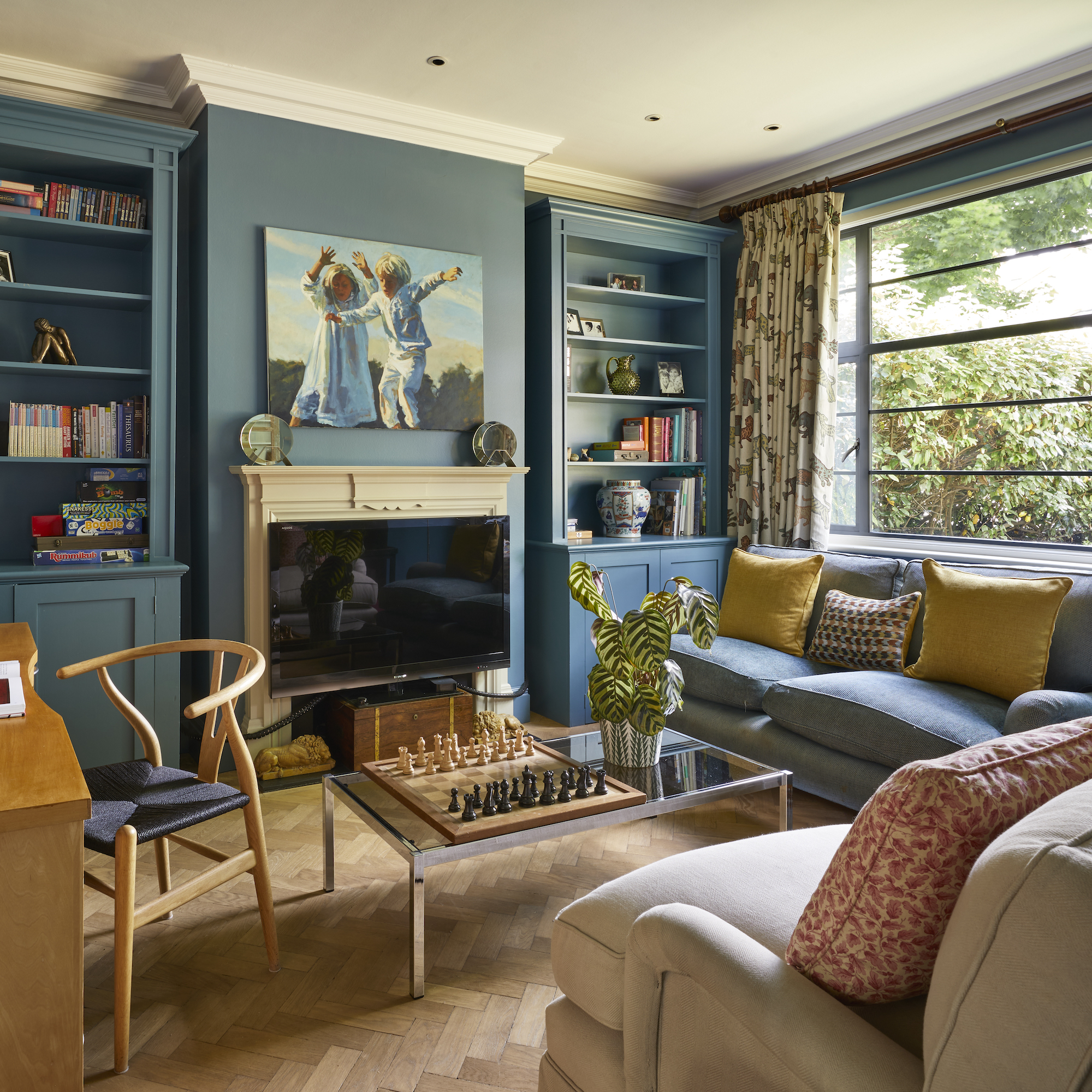 dark blue painted living room with fitted bookshelves in alcoves next to fireplace and coffee table with chess set